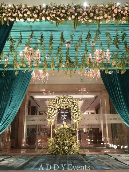 A grand entrance framed by lush teal velvet curtains and a ceiling of hanging florals and chandeliers. This opulent design creates a sense of occasion and luxury, ideal for a high-profile corporate gala or partner event.