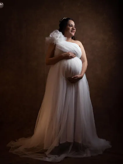 A classic and elegant solo portrait from a studio session. The soft lighting and the beautiful white one-shoulder gown create a timeless, angelic look that focuses on the joy of the mother-to-be.