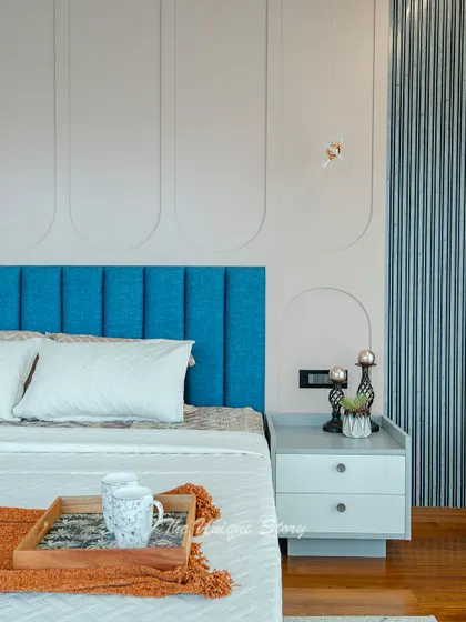 A detail shot of the master bedroom's bedside, showing the vibrant blue headboard against the soft, curved wall paneling. The simple grey nightstand and modern decor create a clean, sophisticated look.