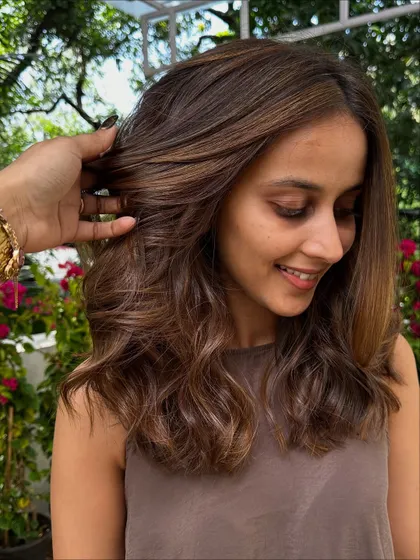A happy client showing off her new face-framing layers and 'Chestnut & Caramel' highlights. The cut is designed to complement the color perfectly.