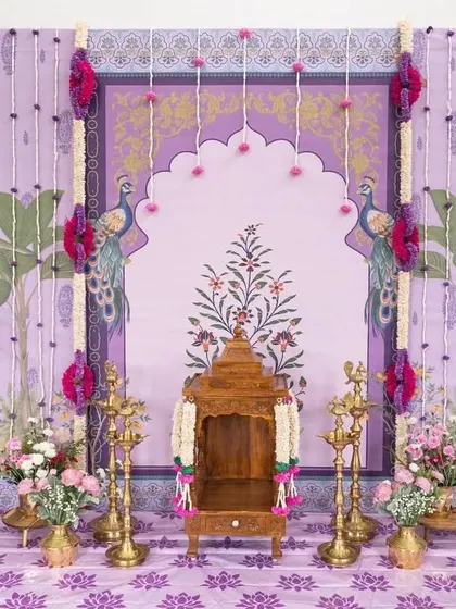 A delicate and beautiful Pichwai-inspired backdrop in shades of lavender. This setup for a small ceremony features a wooden temple (mantapa), brass lamps, and floral accents.