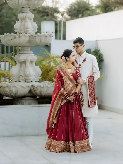A classic portrait of the bride and groom. The bride's deep red lehenga and the groom's white sherwani create a timeless and elegant look.