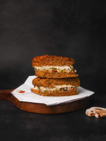 A multigrain sandwich with a creamy filling, stacked on a wooden board against a dark background. The moody lighting creates a sophisticated look for a simple sandwich.
