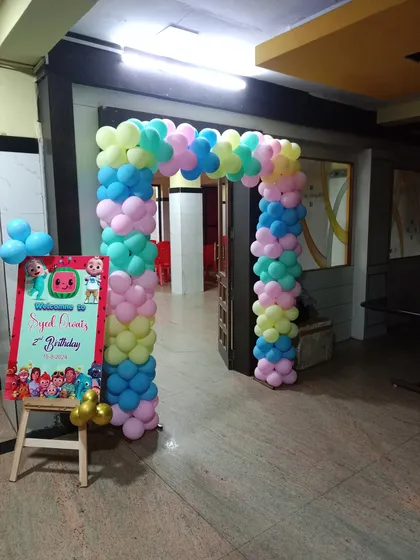 A colorful pastel balloon arch at the entrance to a Cocomelon-themed birthday party. A personalized welcome board greets guests at the door.