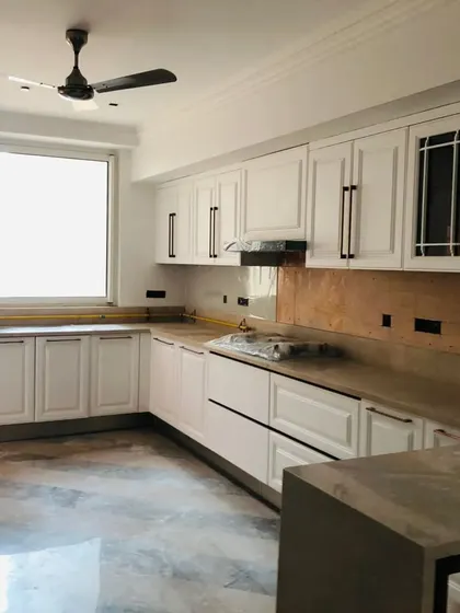 Another angle of the white shaker-style kitchen during installation. The layout provides ample counter space and storage, with a large window bringing in plenty of natural light.