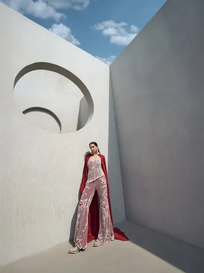 A fully pearl-embellished corset paired with tailored pants. The look is elevated by a floor-sweeping crushed cape that doubles as a dramatic choker, defining elegance with an edge.