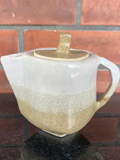 A uniquely shaped hand-built teapot with a clean, modern aesthetic, featuring a two-tone glaze.