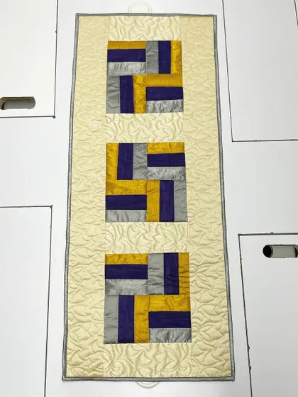 An elegant table runner crafted from shimmering silk fabric in shades of gold, purple, and silver. The luxurious material and intricate quilting make it perfect for special occasions.