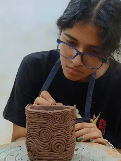 A student creates a swirling texture on her hand-built pot using thin coils of clay. This technique, known as appliqué, adds dimension and visual interest to the surface.