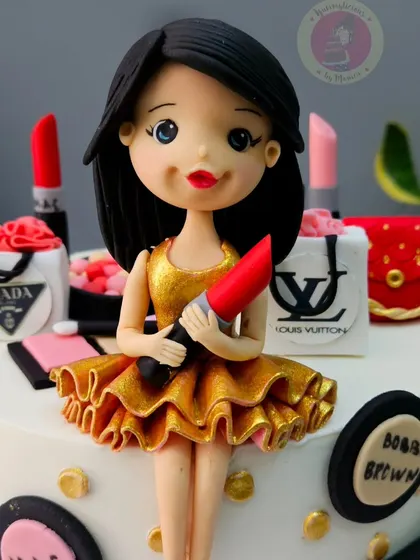 A close-up of the girl figurine on a makeup and shopping themed cake, holding a bright red lipstick.