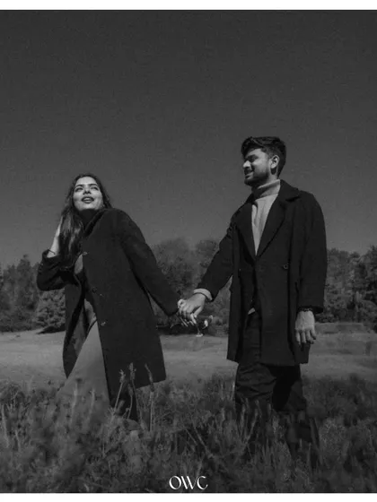 A candid and joyful black and white photo of a couple walking through a field, capturing a moment of pure happiness.