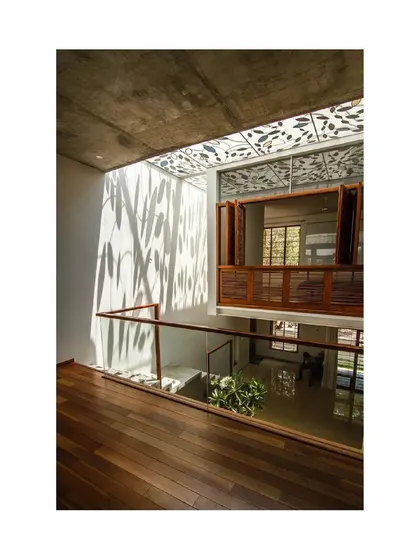 A custom-designed skylight in 'Cube Square' casts leaf-like shadows onto the walls, creating a poetic play of light. This feature, combined with the wooden shutters and flooring, adds warmth and intricate detail to the upper-level living space.