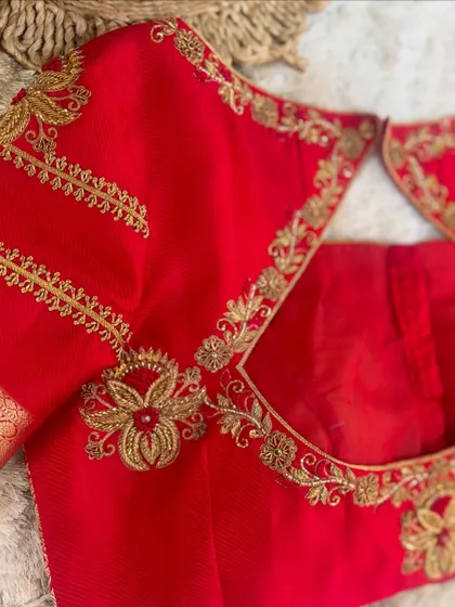 A close-up of the neckline and sleeve of the red blouse, highlighting the fine details of the zardosi work.