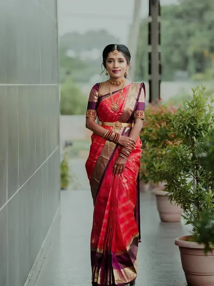 A client looking elegant in a vibrant red silk saree, paired with a custom-designed purple blouse with gold embroidery.