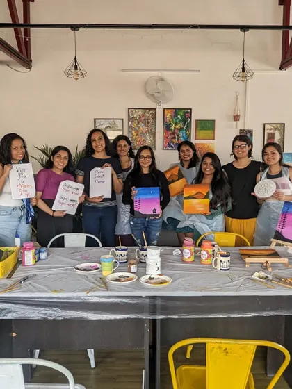 A group of happy participants with their finished canvas paintings, calligraphy cards, and Lippan art.