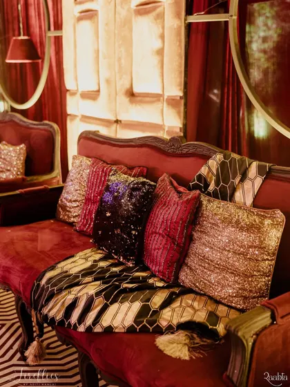 A luxurious lounge sofa at 'The Scarlet Soirée', adorned with sequined and velvet cushions in rich, dramatic tones.