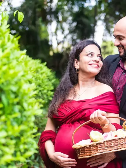 A beautiful portrait of an expecting couple surrounded by nature. The mother-to-be holds a basket of flowers, adding a soft and romantic element to the scene.
