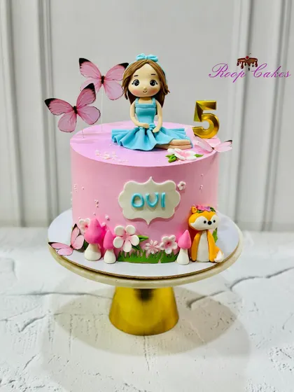 A pretty pink 5th birthday cake featuring a custom doll, a friendly fox, and a garden of mushrooms and flowers.
