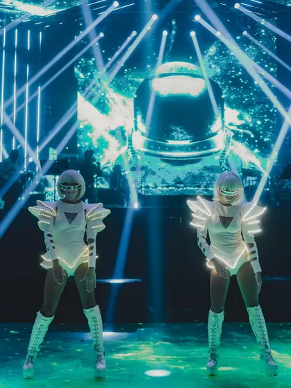 Dancers in futuristic white costumes with LED light strips perform on stage. The choreography and costumes were designed to perfectly match the event's space-age theme.