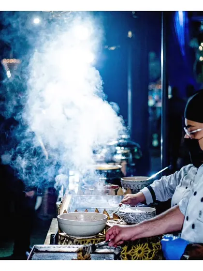 A dramatic, smoky shot of our live dosa station, capturing the sizzle and steam as the batter hits the hot plate.