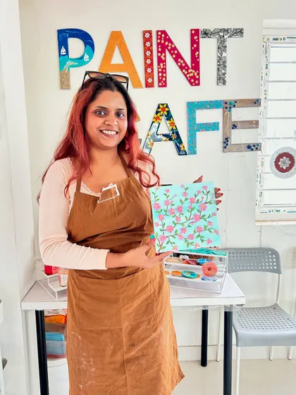 A participant in an apron holds up her lovely floral canvas painting.