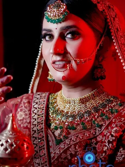 A classic bridal portrait with the bride holding a traditional pot (karwa), shot with dramatic red lighting for a powerful effect.