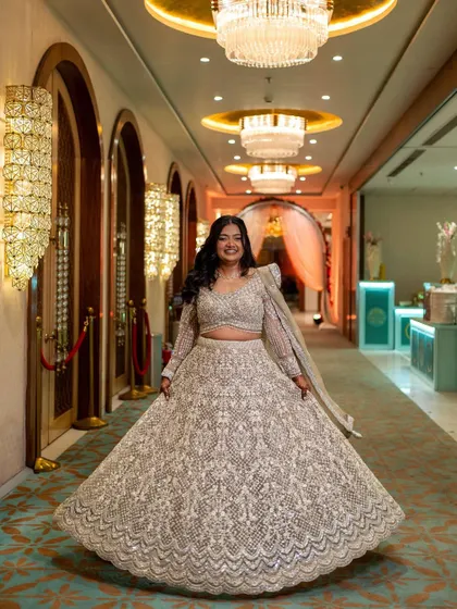 A full-length shot showing the stunning silver lehenga. The minimal and glowing makeup perfectly complements the intricate details of her outfit.