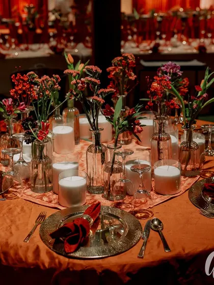 A table set for a royal-themed wedding dinner. The hammered metal charger plate, deep red napkin, and simple floral arrangement create a look of understated opulence.