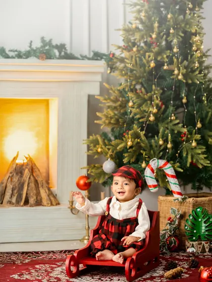 A happy baby enjoying his sleigh ride by the Christmas tree and a cozy fireplace.