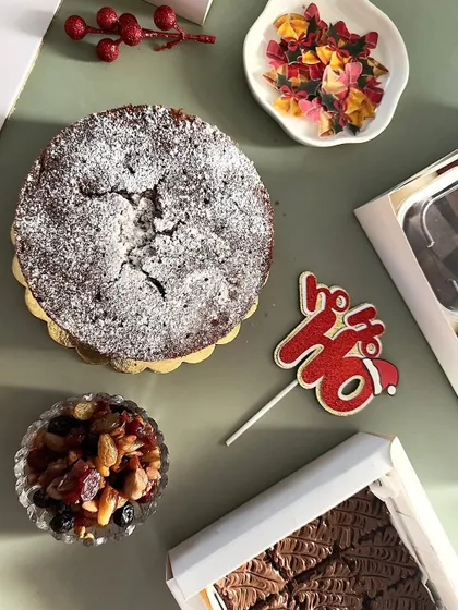 A festive flatlay of some of my Christmas specials. You can see my classic plum cake dusted with powdered sugar, a box of brownies, and a bowl of the rich dried fruits I use in my baking.
