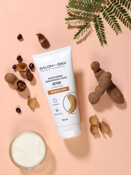 This is a top-down product photograph for a tamarind and curd-based de-tan cream. The composition includes the raw ingredients to clearly message the product's natural formulation.
