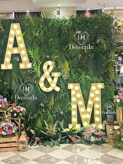 Another view of the engagement photo wall, showing the beautiful contrast between the green foliage and the warm light of the marquee letters.
