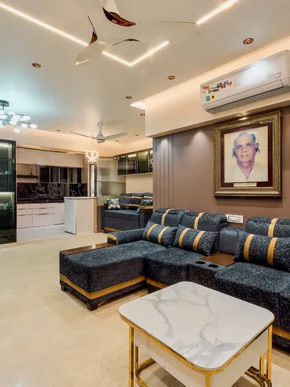 A luxurious living room with a custom L-shaped sofa with gold accents, a marble-top center table, and an open-plan layout connecting to the kitchen.