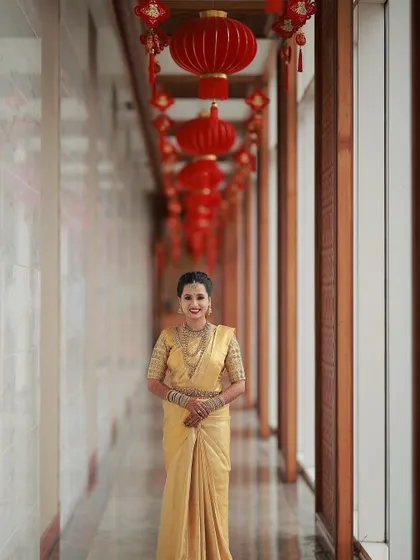A stunning full-length shot of Manjushri in a golden Kanchipuram saree. Her makeup, featuring a bold red lip, creates a striking and regal look perfect for a grand wedding.