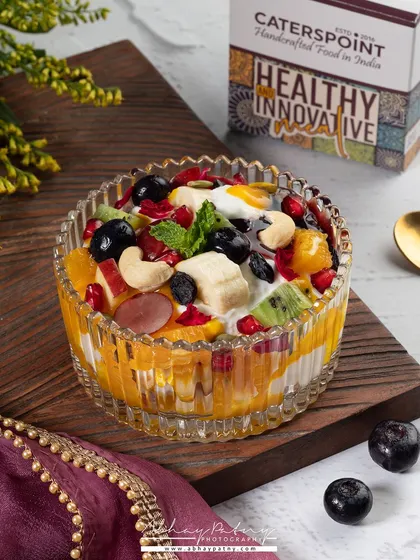 A beautiful crystal bowl filled with fresh fruit salad. The lighting from the side highlights the glistening texture of the fruits, making them look juicy and fresh.