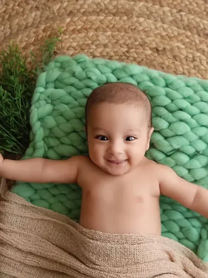 An overhead shot of a smiling baby lying on a green knitted blanket over a jute rug.