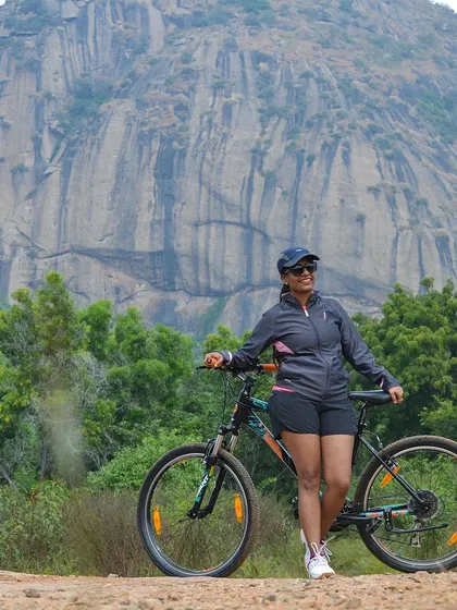 A cyclist posing with her bike against the backdrop of the iconic Ramanagara hills, famous from the movie 'Sholay'.