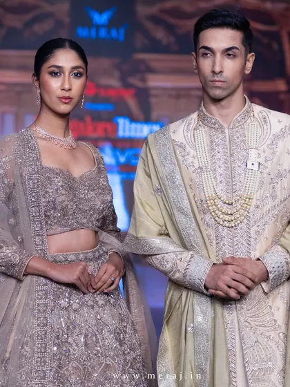 A close-up of the runway couple, showing the detail in the groom's gold raw silk sherwani. The zardosi hand embroidery and pearl mala create a look of pure royalty.
