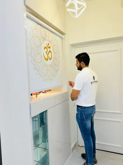 This foyer mandir features a custom printed blind with a mandala and 'Om' design, which can be rolled down for privacy. The unit is finished in high-gloss white with elegant moulding.