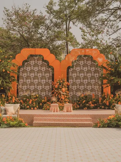 The main stage for the Haldi, featuring two large orange arches with a custom block-print backdrop, surrounded by lush orange flowers and real orange trees.