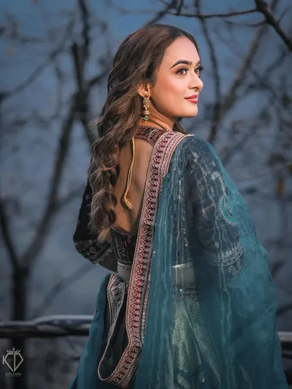 An elegant portrait from behind, showcasing the beautiful details of her traditional lehenga and her graceful profile against the evening sky.