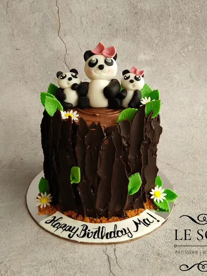 A sweet panda-themed cake for a mom's birthday. This 1 kg Vanilla Caramel cake features a chocolate bark tree stump design and an adorable family of fondant pandas.