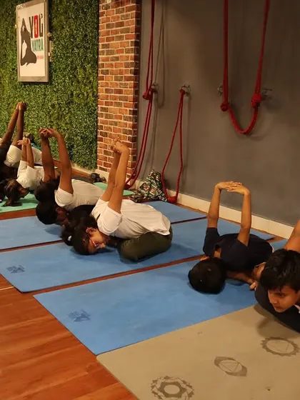 A row of students practicing a seated hip-opening pose, working on flexibility in a controlled and mindful way.