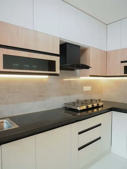 This L-shaped kitchen features a two-tone design with light wood-finish upper cabinets and off-white lower cabinets. The concealed handles and under-cabinet lighting contribute to a clean, modern aesthetic.