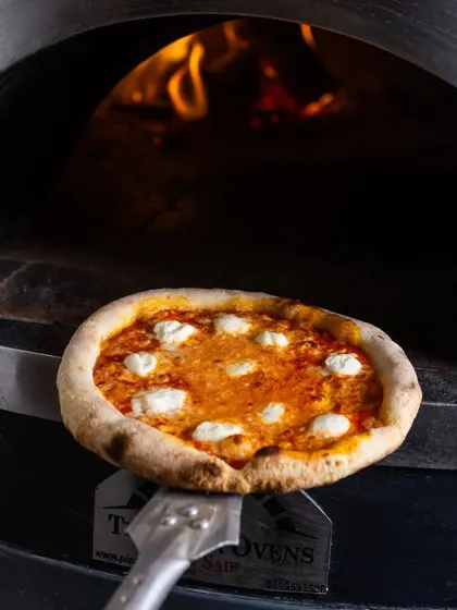 A classic cheese pizza on a peel, with the fire glowing warmly in the background. This shot captures the essence of my pizzeria: simple, authentic, and delicious.