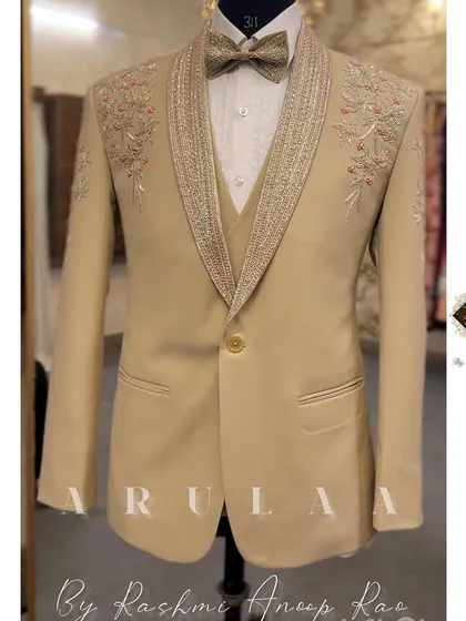 This beige three-piece suit offers a softer, elegant alternative for a day wedding or reception. The design features delicate floral embroidery on the shoulders and a richly detailed lapel, combining classic tailoring with romantic touches.