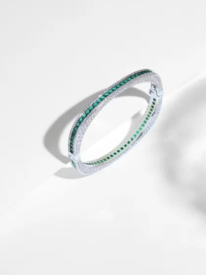 This 14k gold bangle showcases a modern, geometric design. It features a line of princess-cut emeralds bordered by round-cut diamonds, perfect for those who love quiet luxury.