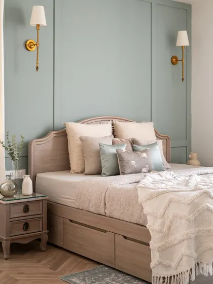 A bedroom in our Riviera Maison project, featuring a soft sage-green paneled wall and a custom bed with built-in storage drawers. The brass wall sconces add a touch of classic elegance.