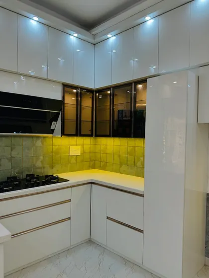 The 'after' shot of a major kitchen renovation. The all-white high-gloss cabinets, combined with a textured green backsplash and under-cabinet lighting, create a bright and luxurious space.