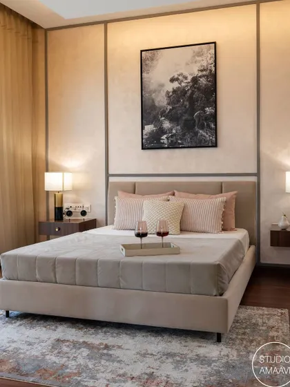 A closer look at the bed from the previous image, this shot highlights the serene color palette of beige and soft pink. The textured wall panels with metallic trim add a subtle touch of luxury, while the tray with wine glasses suggests a space designed for ultimate relaxation.